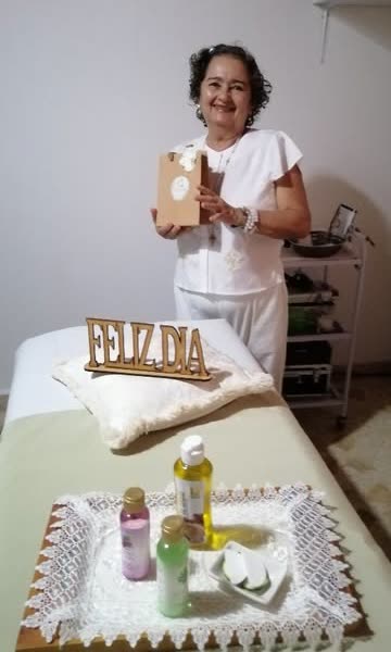 Clienta con su bolsa de regalo junto a la camilla con aceites y el letrero Feliz día
