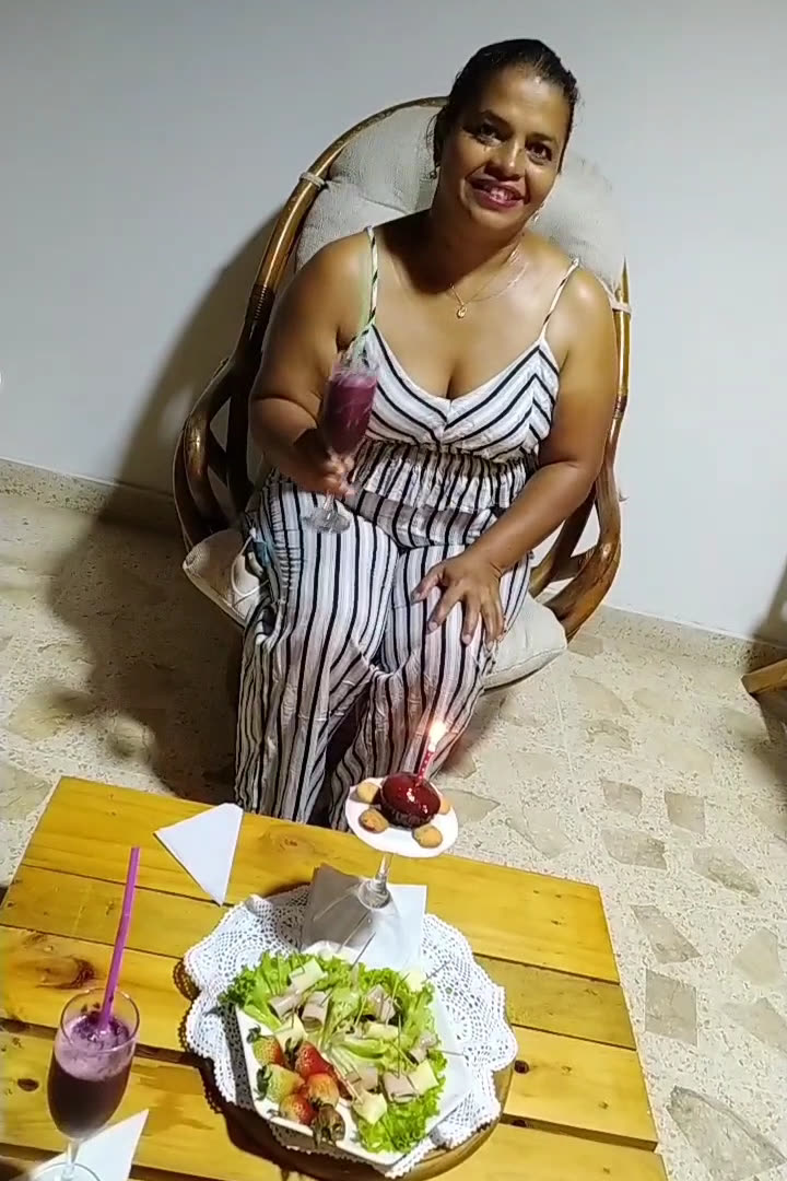 Clienta sonriente junto a un plato fresco y un jugo en una mesa de madera