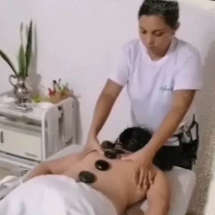 Terapeuta dando masaje con piedras oscuras sobre la espalda